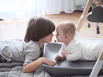 Baby laying on stomach on a changing pad playing with toddler boy